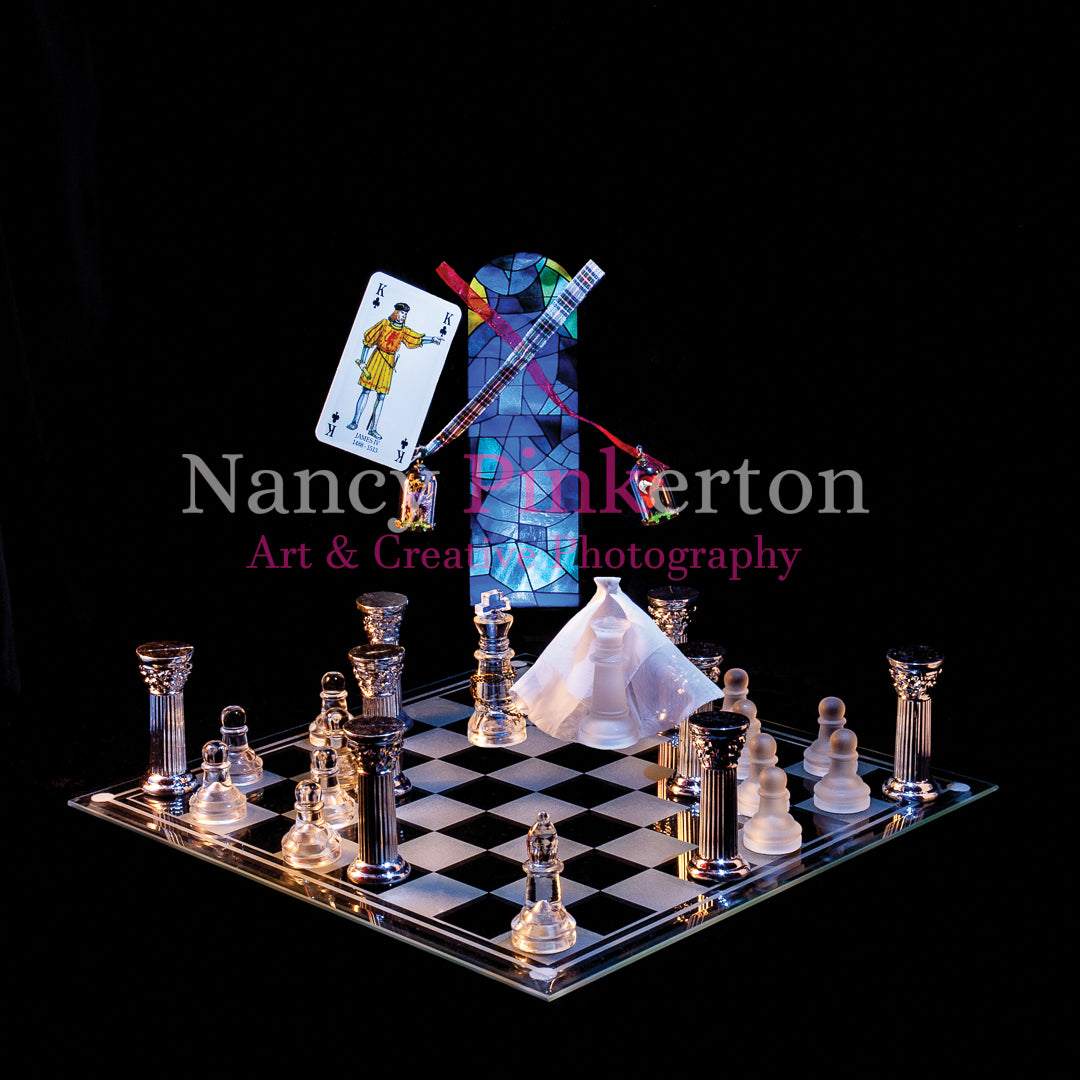 Photographic art print with image of a playing card featuring King James IV floating next to a thistle and a rose just above a king and queen with a white veil above a glass chessboard laid out with silver pillars and chess pieces.