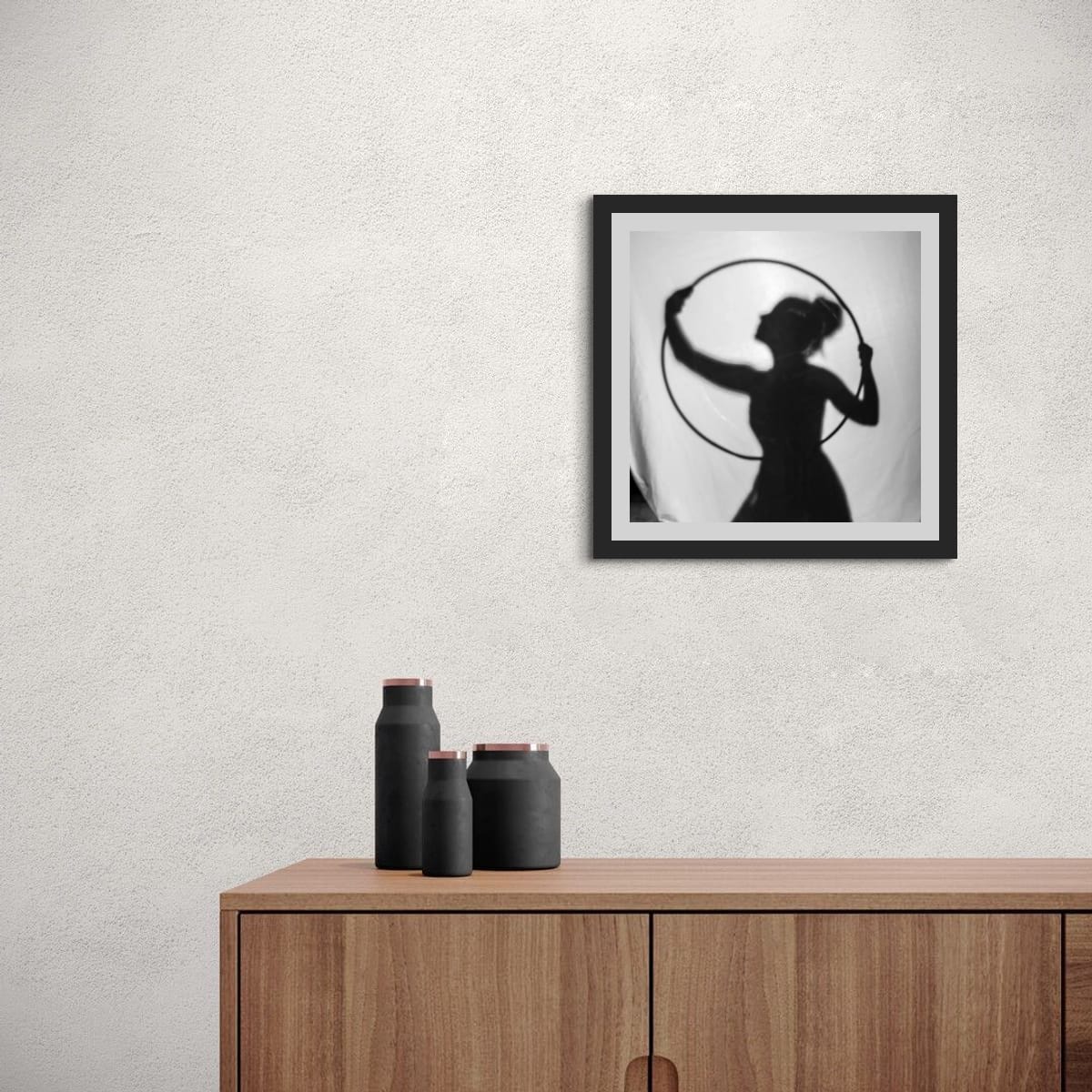 Framed black and white silhouette art on a wall above a wooden cabinet with black vases.