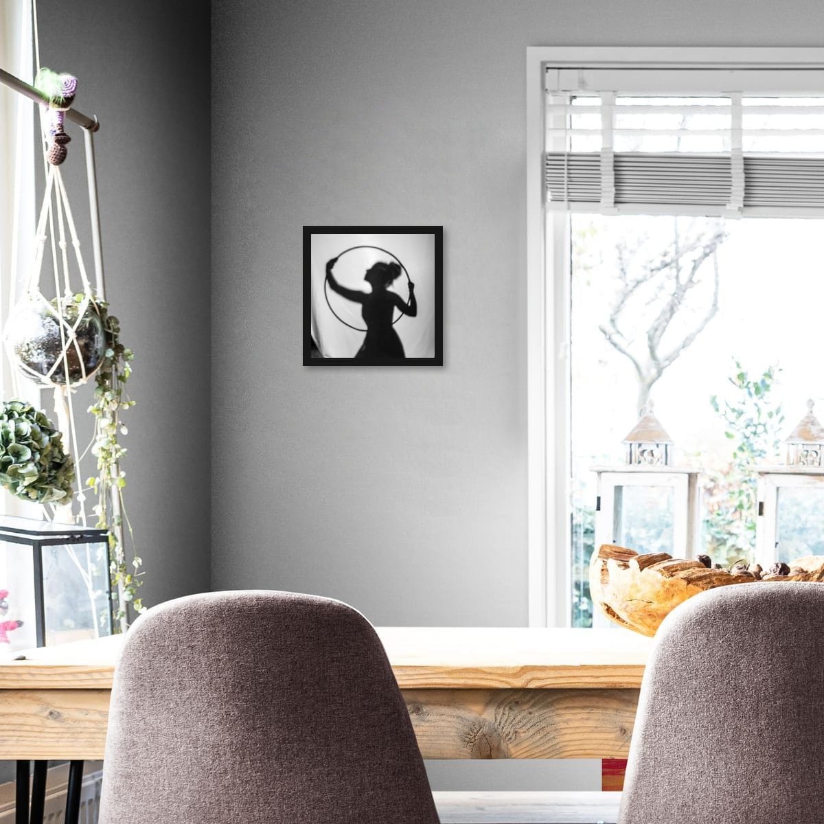 Framed silhouette art on a gray wall above a wooden table with chairs.