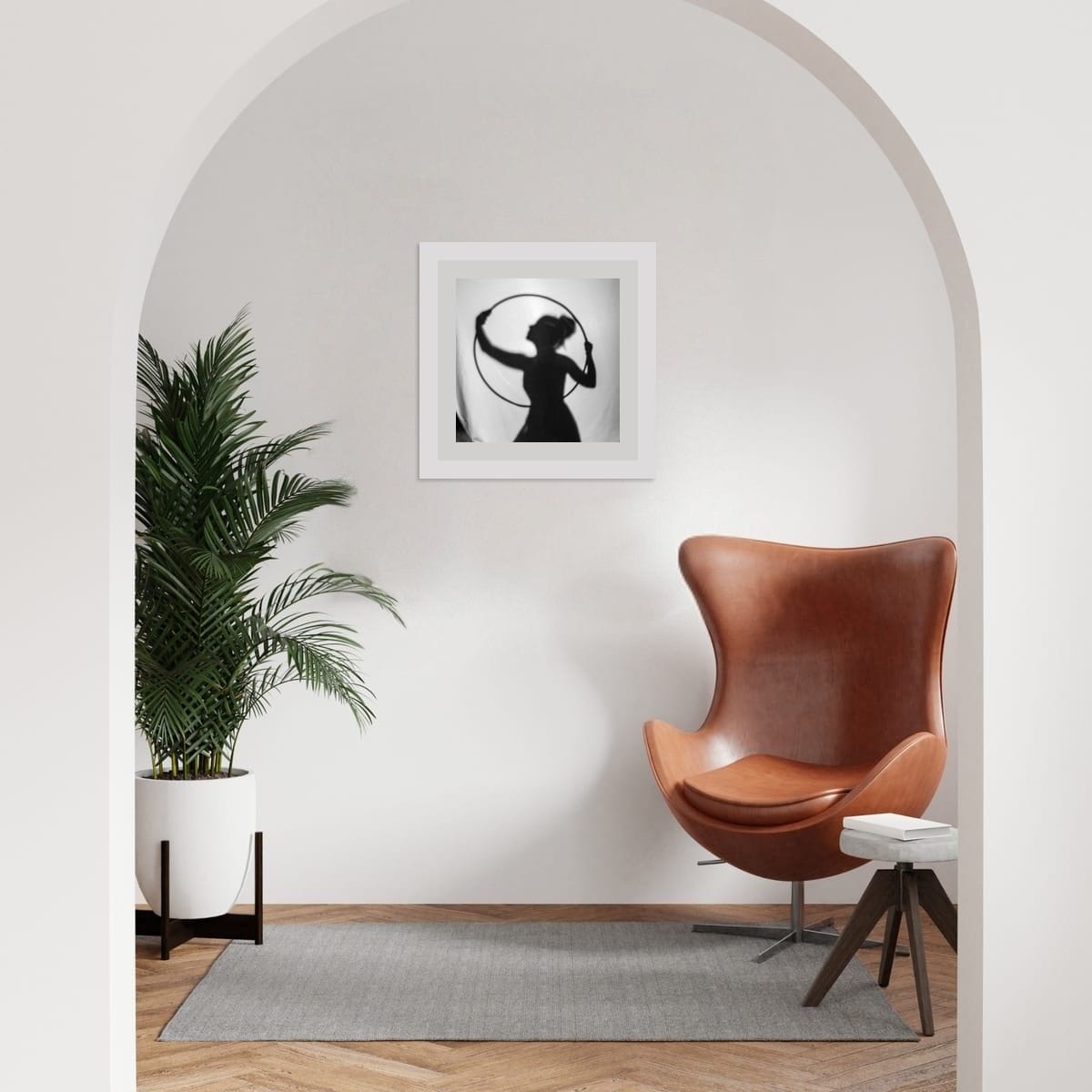 Modern interior with a brown leather chair, plant, and framed artwork on a white wall.