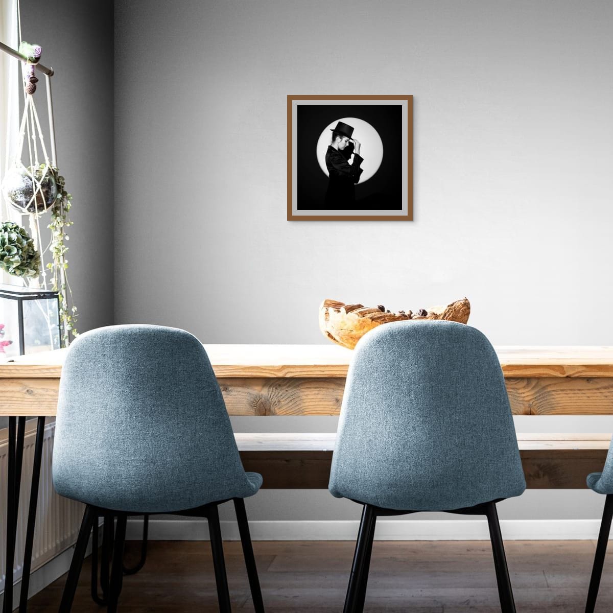 Two blue chairs in front of a wooden table with a framed black and white portrait 'In the Spotlight' on the wall.