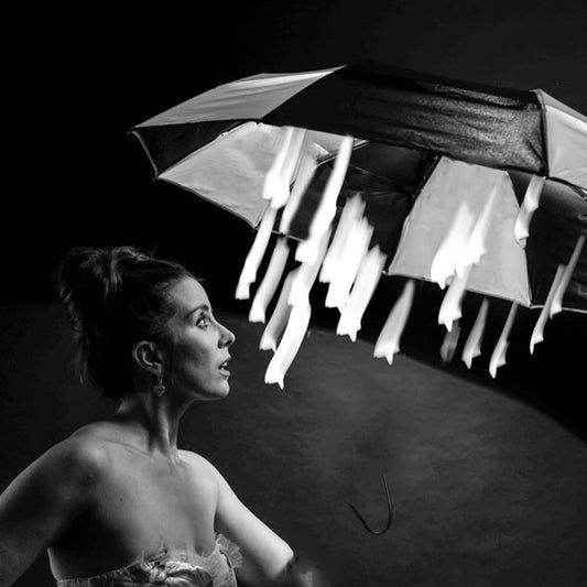 Black and white photo of a woman looking up at a black and white umbrella with starlight falling from the umbrella