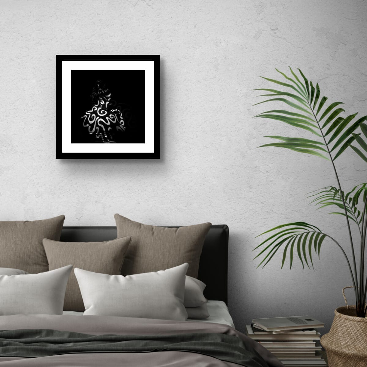 Framed black and white artwork Tattooed by light above a bed with pillows and a plant on a gray wall.