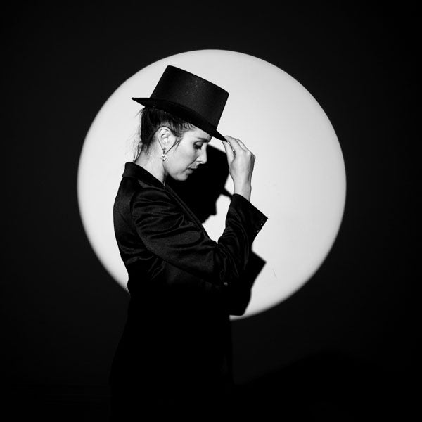 Person wearing a black hat and coat with a circular light source in the background