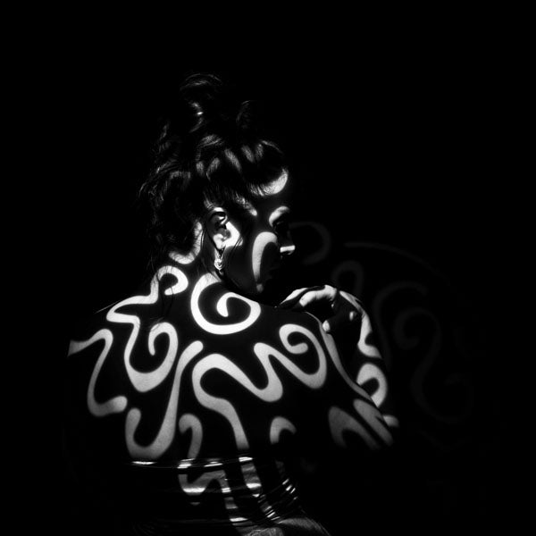 Person with white abstract patterns light projected on to her back on a black background