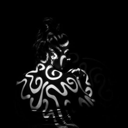 Person with white abstract patterns light projected on to her back on a black background